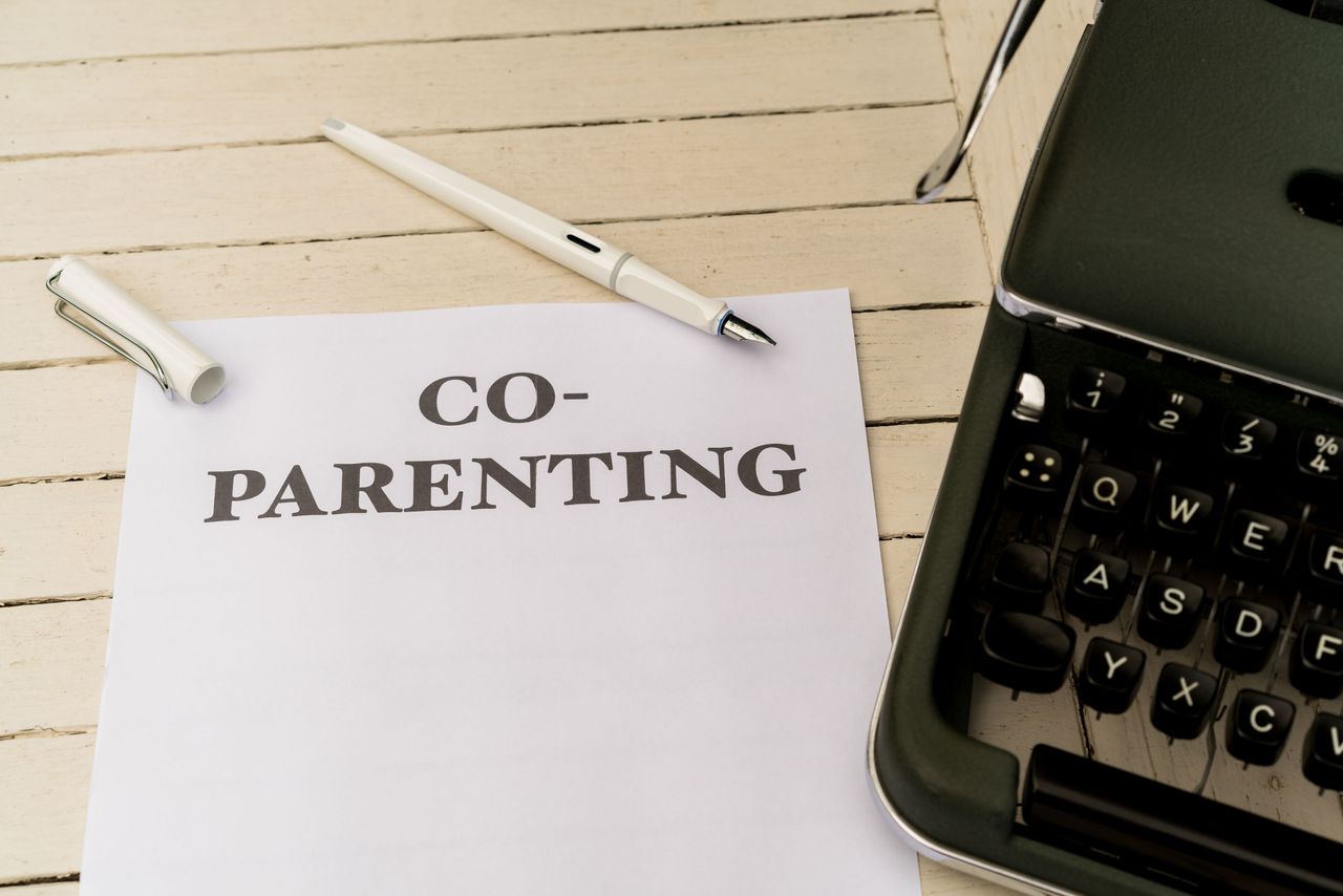 Co-parenting paper and pen on a white wooden table next to a typewriter.