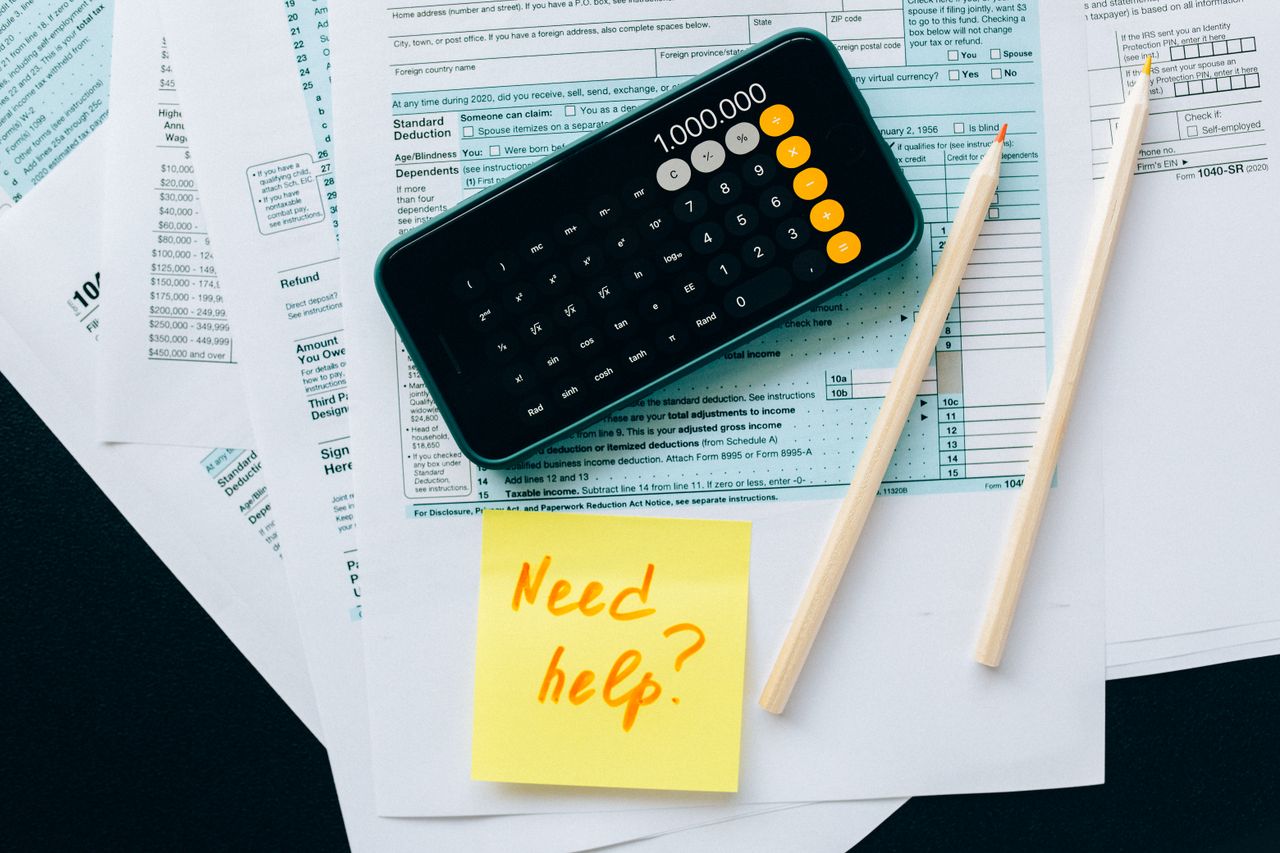 Crafting Captivating Headlines: Your awesome post title goes here Top view of financial papers with a calculator, pencils, and a note saying 'Need help?' indicating tax or accounting assistance.