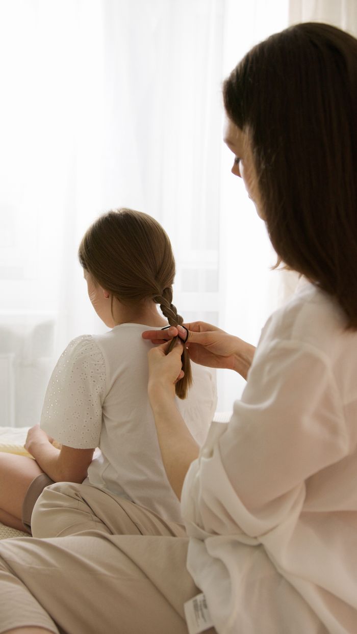 A mother lovingly braids her daughter's hair in a bright, sunlit room, capturing a tender family moment.